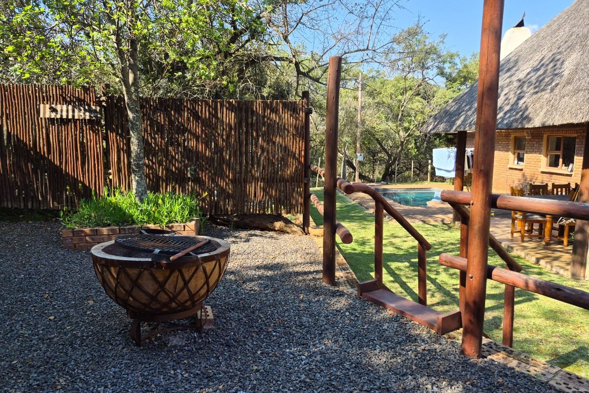 Rear garden area featuring a swimming pool, thatched roof structure, timber fencing, and a gravel patio space.