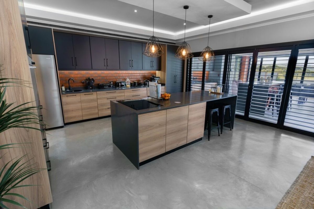 Modern kitchen featuring two-tone cabinetry, a central island with integrated cooktop, polished concrete flooring, and recessed ceiling lighting with a brick backsplash.