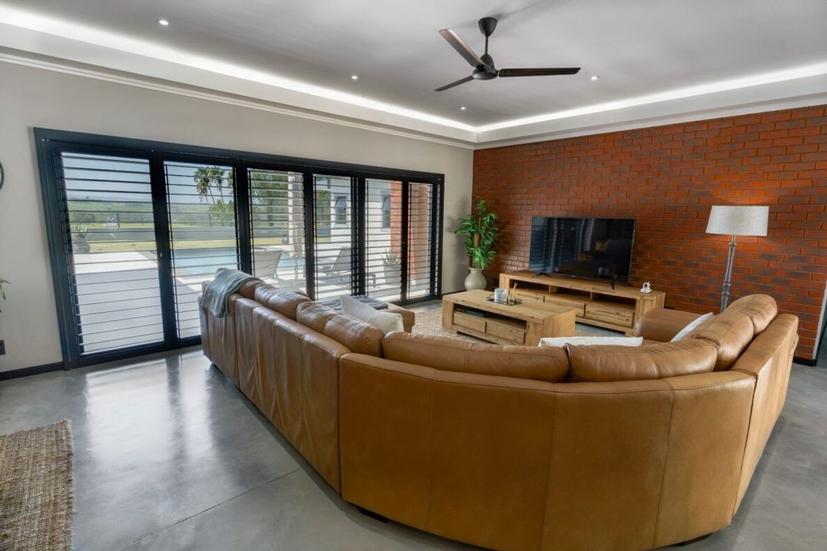 Spacious living room featuring a striking exposed brick feature wall, polished concrete flooring, recessed ceiling lighting, and large sliding doors opening to the pool area.