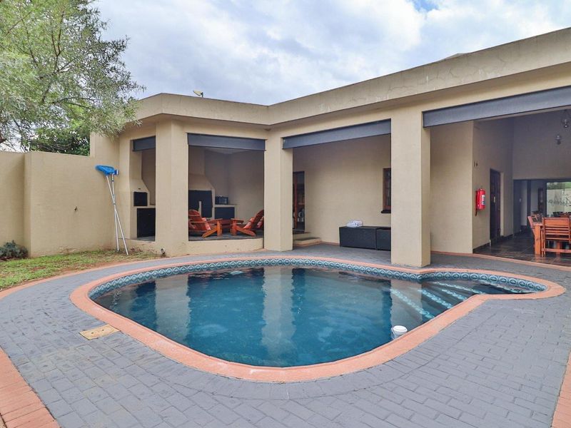 Outdoor entertainment area featuring a covered patio with built-in braai, overlooking a swimming pool with paved surround.