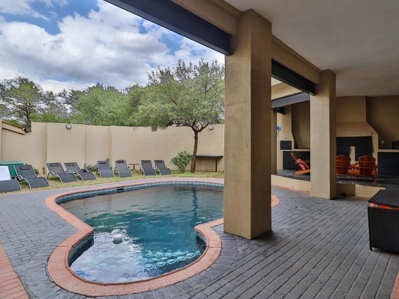 A covered patio area featuring a built-in braai, overlooking a swimming pool and a private garden with perimeter walling.