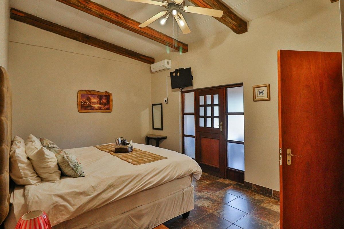 A bedroom featuring exposed wooden ceiling beams, tiled flooring, and a wooden door with glass panels leading to an exterior area.