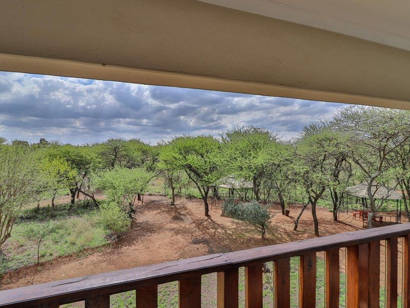 A view from a covered balcony overlooking a natural farm landscape with mature trees and outdoor structures.