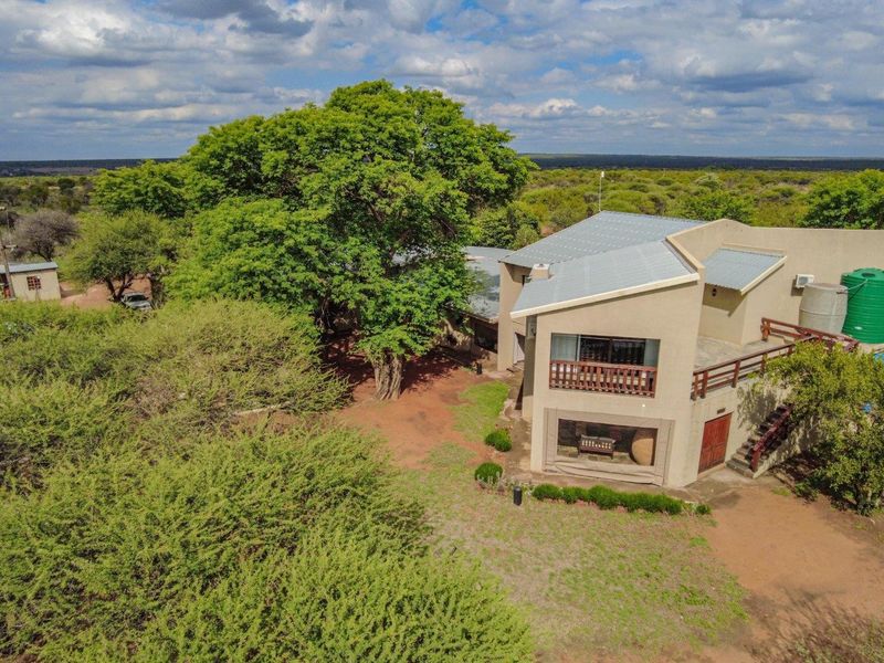 Aerial view of a multi-level farm residence featuring a metal roof, upper-level balcony, and an external water storage tank set within a rural landscape.