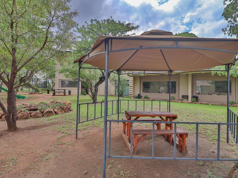 Spacious garden area featuring a metal gazebo structure, established trees, and a rock-bordered garden bed, providing a pleasant outdoor setting.