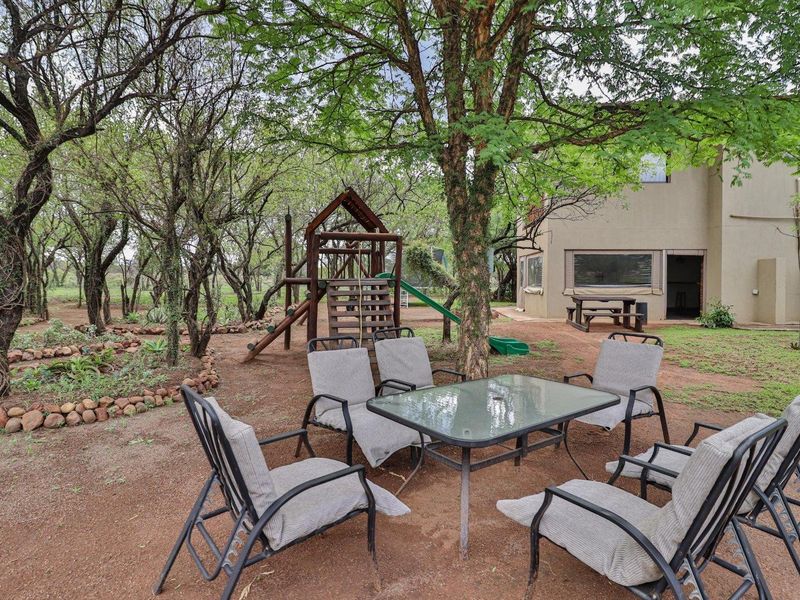 A spacious rear garden area featuring mature trees, a wooden play structure, and a natural earth ground cover adjacent to the main dwelling.