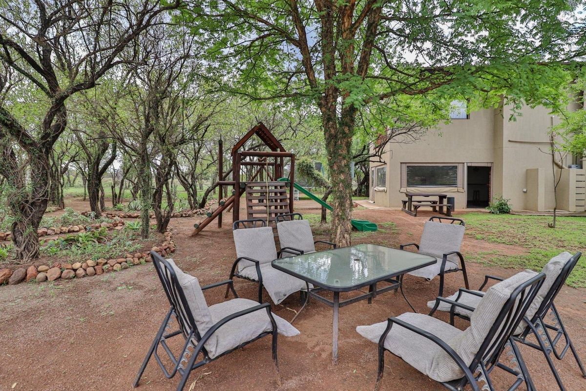A spacious rear garden area featuring mature trees, a wooden play structure, and a natural earth ground cover adjacent to the main dwelling.