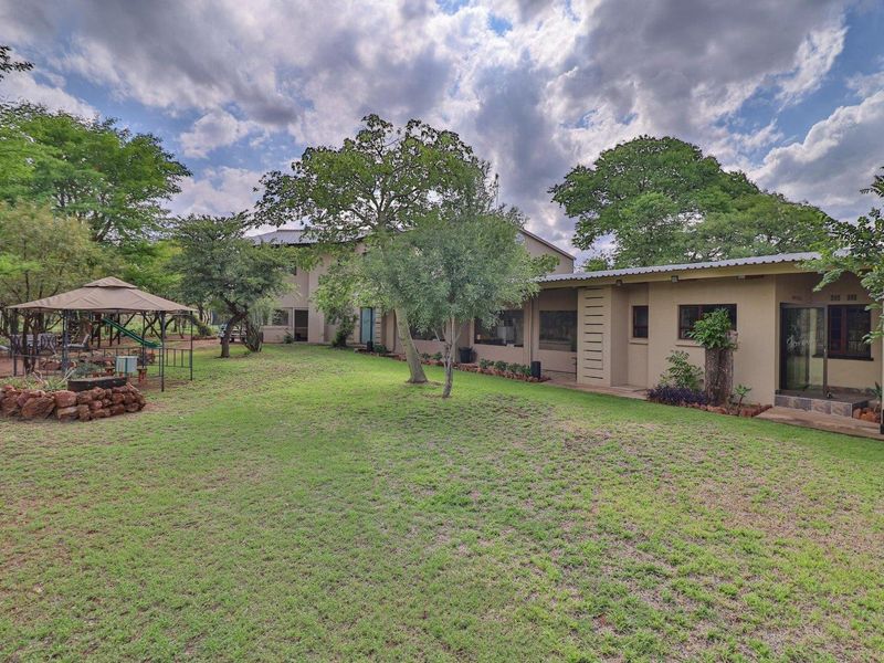A view of the rear exterior of the farm property, featuring a large lawn, mature trees, and a covered patio area.