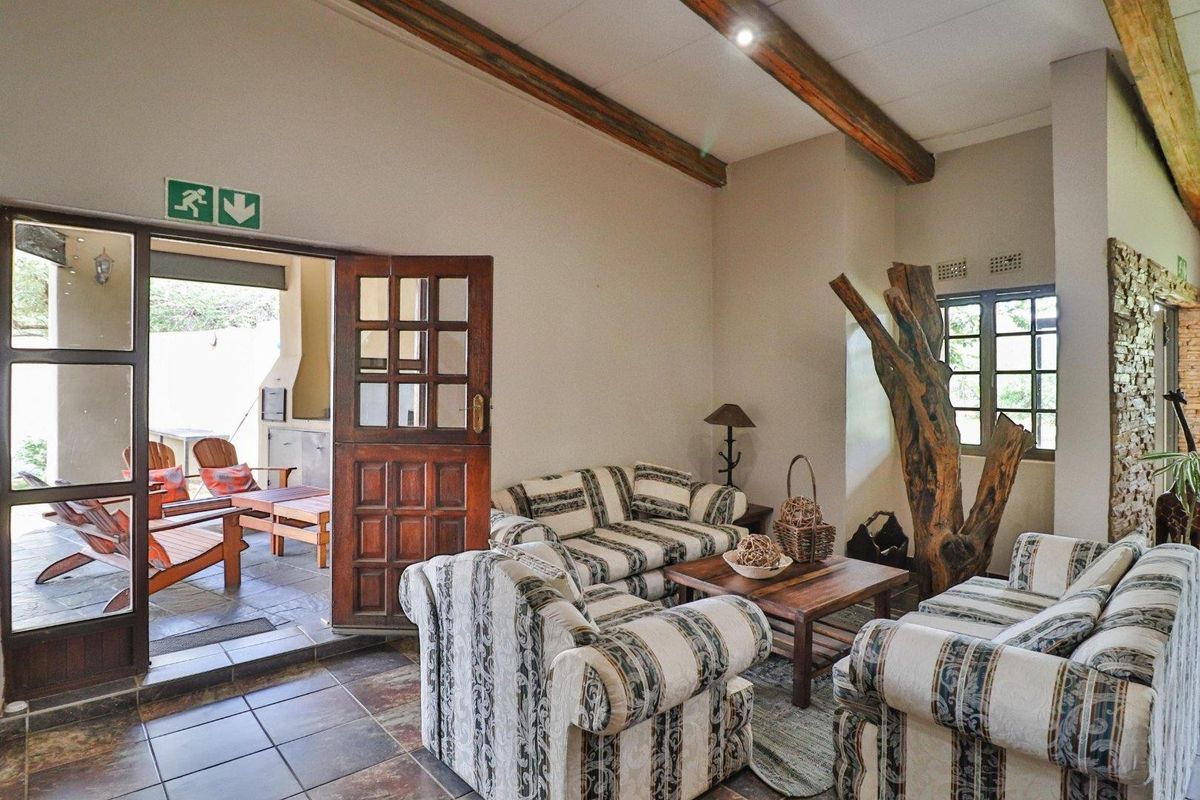 A rustic living room featuring exposed timber ceiling beams, tiled flooring, and direct access to an outdoor patio area.