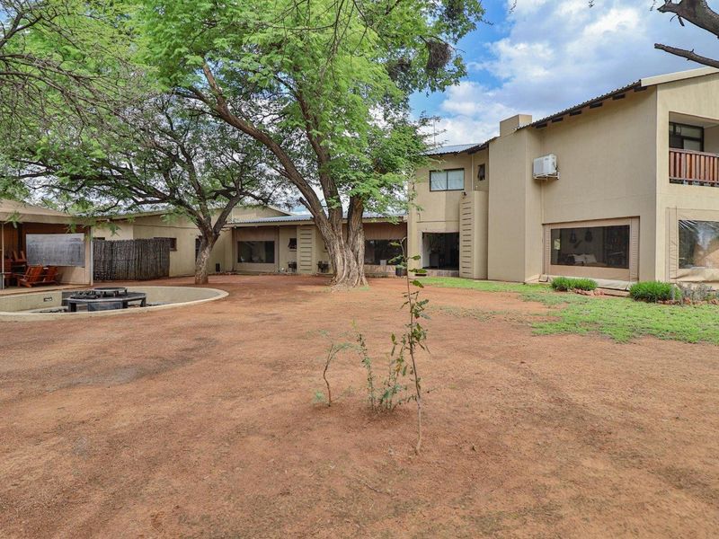 Spacious rear exterior view of the farm property featuring a large open yard, mature trees, a circular fire pit, and a multi-level building structure.