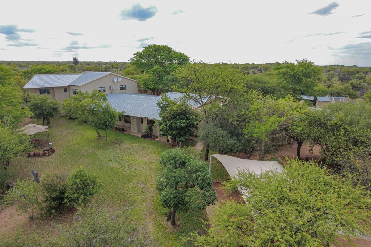 An aerial view of the farm property, showcasing the main dwelling, surrounding landscaped garden, mature trees, and a shaded outdoor area.