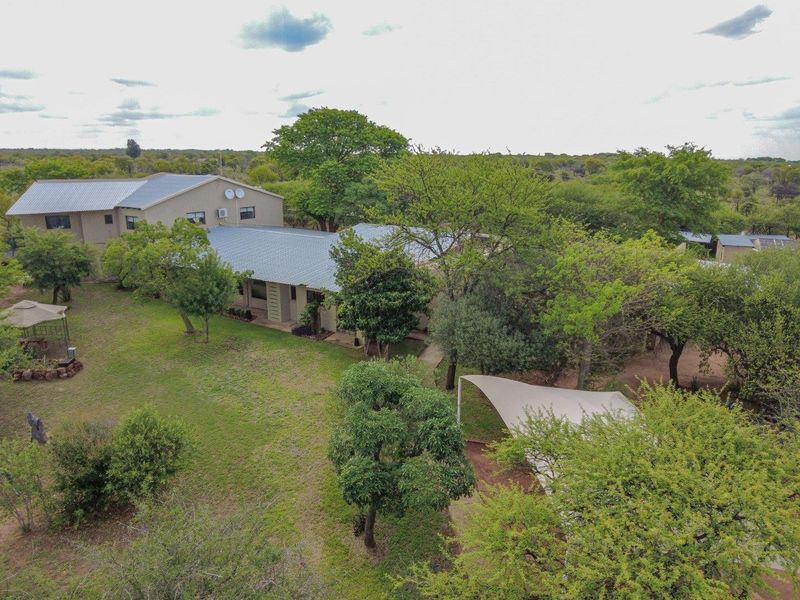 An aerial view of the farm property, showcasing the main dwelling, surrounding landscaped garden, mature trees, and a shaded outdoor area.
