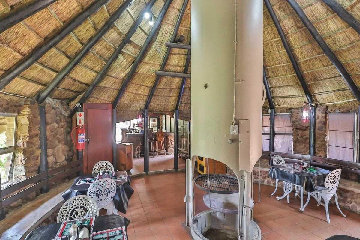 Rustic entertainment area featuring a central built-in fireplace, exposed thatch roof, stone wall accents, and tiled flooring in a farm-style setting.