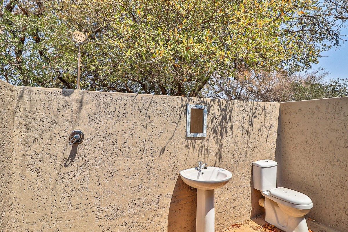 Outdoor bathroom area featuring a wall-mounted shower, pedestal basin, and toilet set against a rustic textured wall.