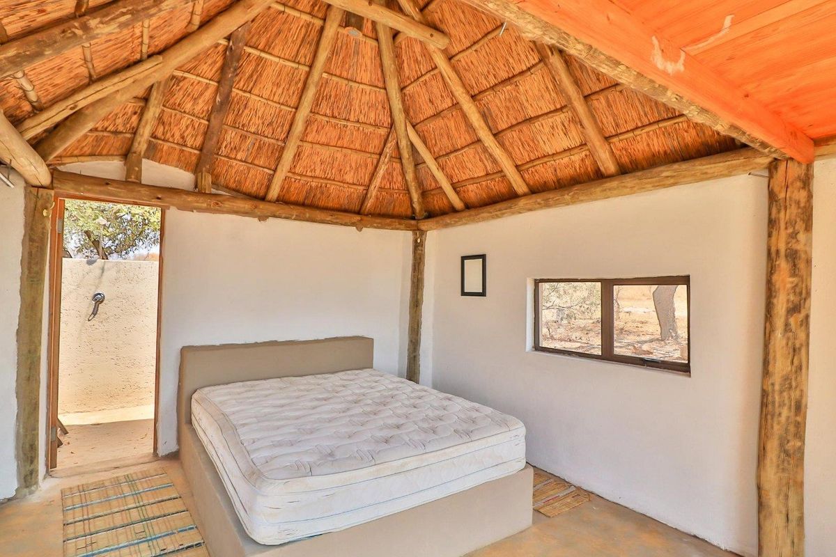 Rustic bedroom featuring a traditional thatched roof, exposed timber support beams, and direct access to an outdoor area.