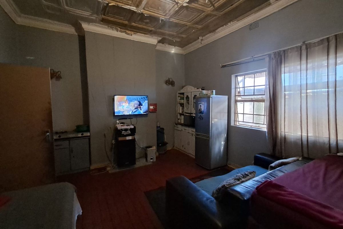A living area featuring a decorative pressed metal ceiling, timber flooring, and a window with security bars.