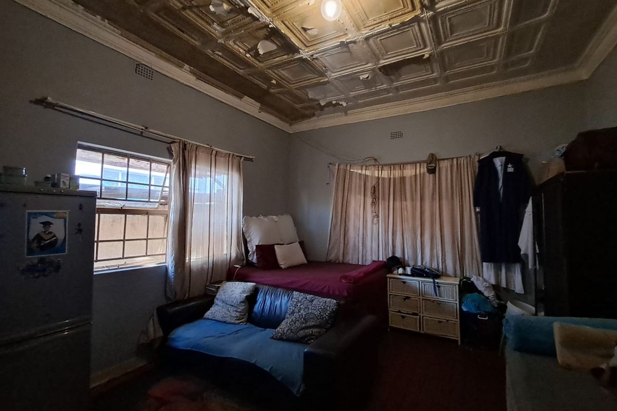 A bedroom featuring a decorative pressed metal ceiling in need of repair, with standard window fixtures and basic interior finishes.