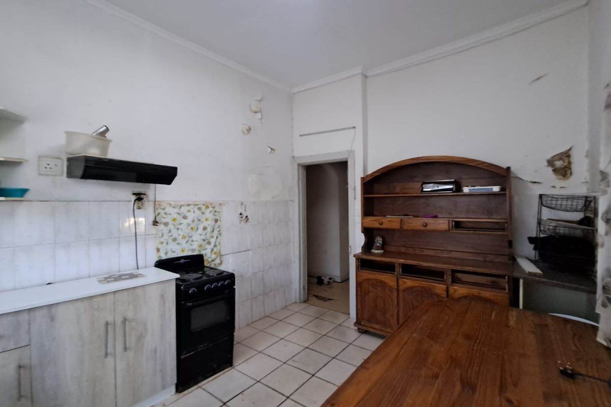 A dated kitchen featuring tiled flooring, basic cabinetry, and a freestanding stove, requiring significant cosmetic renovation and wall repairs.