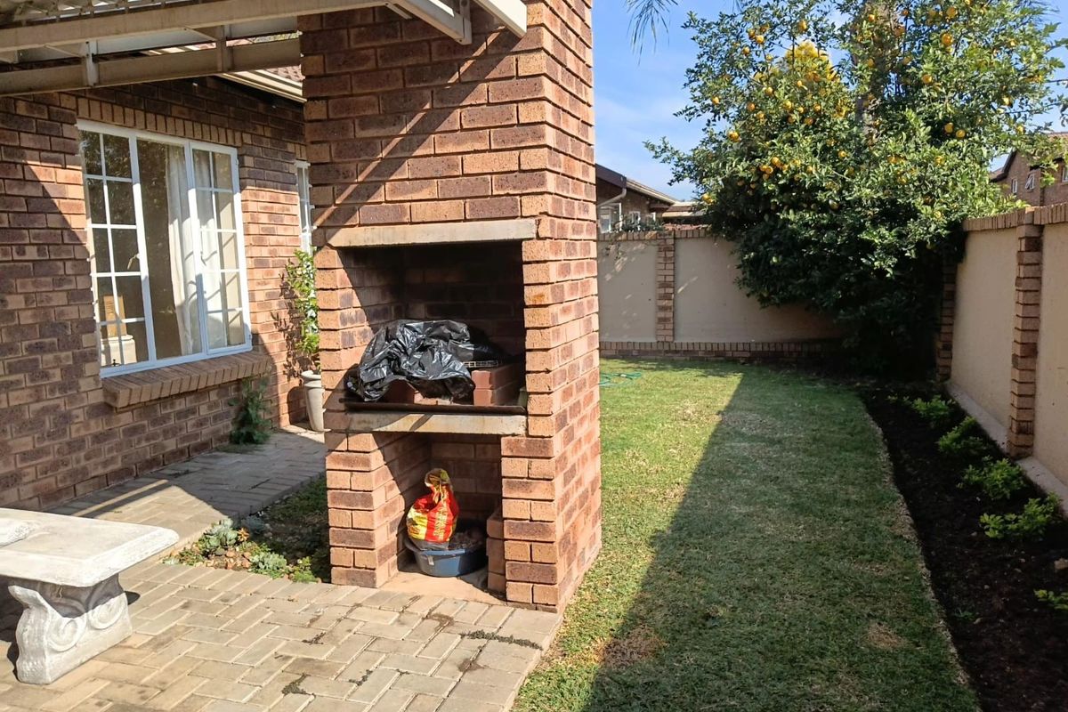 A private rear garden featuring a built-in brick braai, paved patio area, and established lawn, perfect for outdoor entertaining.