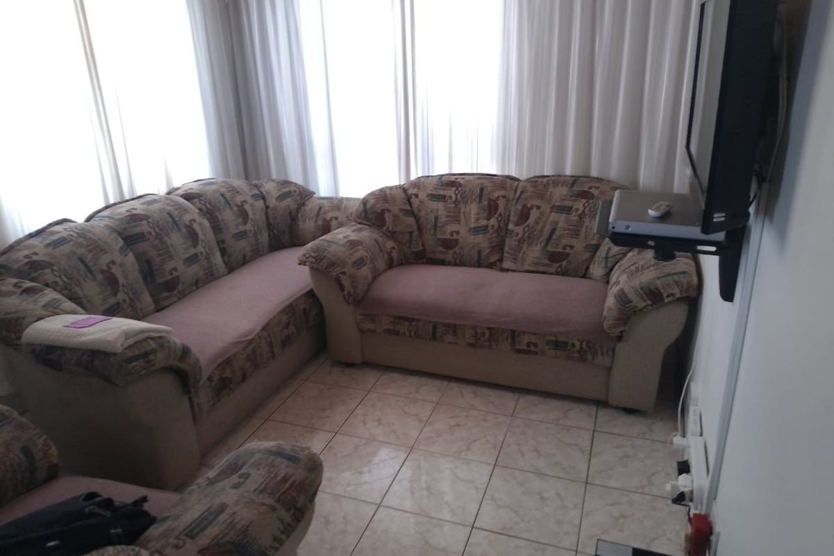 A living room area featuring tiled flooring and large windows with curtains, providing a functional space for relaxation.