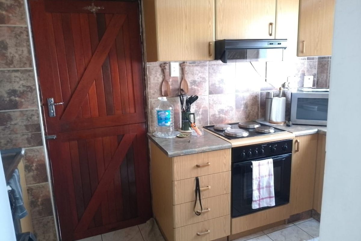 Compact kitchen featuring light wood-finish cabinetry, tiled backsplash, and a built-in electric oven with extractor fan, adjacent to a solid timber stable-style door.