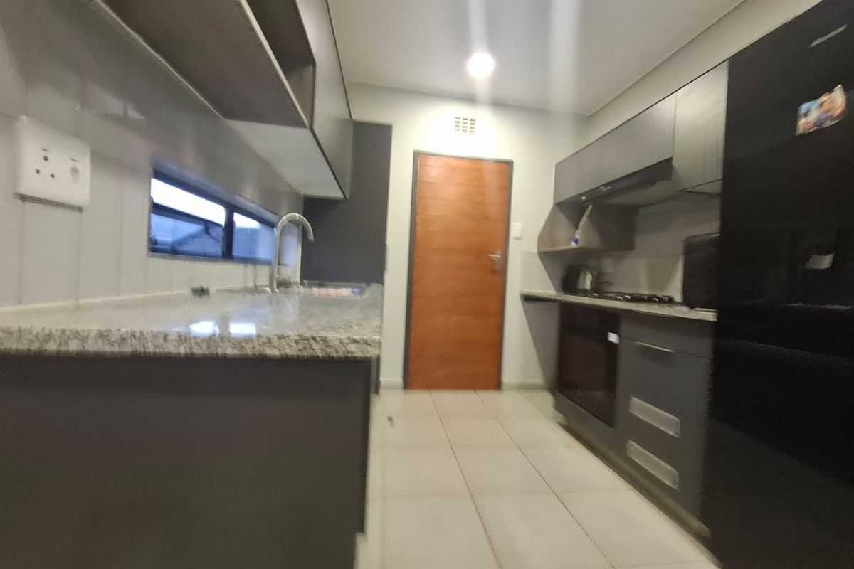 Modern galley-style kitchen featuring granite countertops, dark cabinetry, built-in oven, gas hob, and tiled flooring.