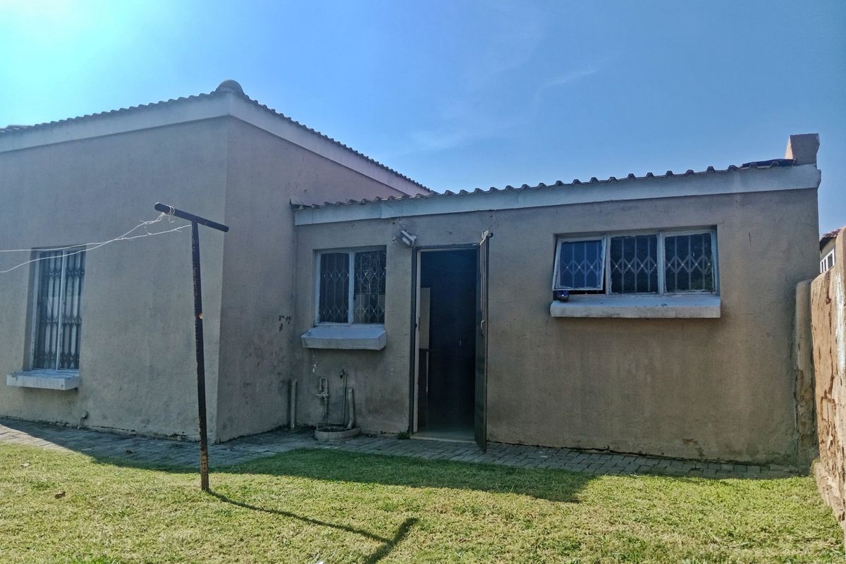 Rear view of the property featuring a paved walkway, security bars on windows, and a small lawn area.