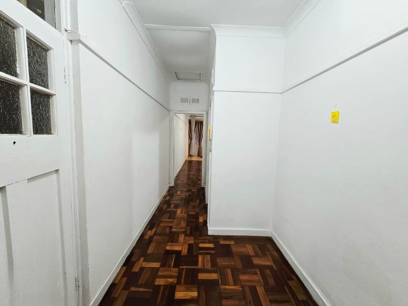 A bright, empty hallway featuring classic parquet flooring, white walls with coved cornicing, and a traditional timber door with glass panels.