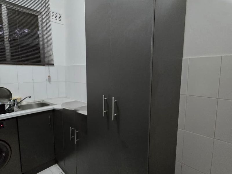 A functional laundry room featuring built-in dark cabinetry, a stainless steel sink, tiled splashback, and tiled flooring.