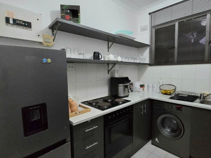 Compact kitchen featuring dark cabinetry, built-in oven and hob, tiled flooring, and open shelving for storage.