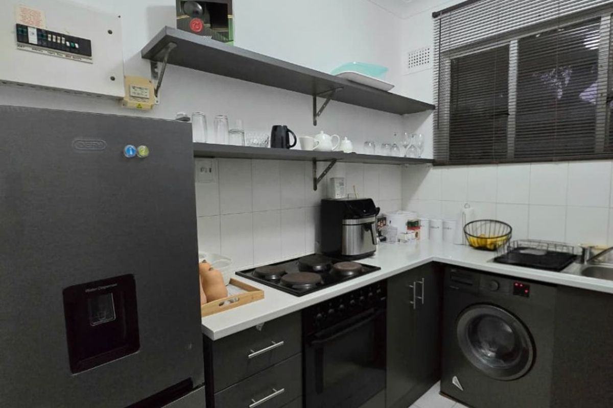 Compact kitchen featuring dark cabinetry, built-in oven and hob, tiled flooring, and open shelving for storage.