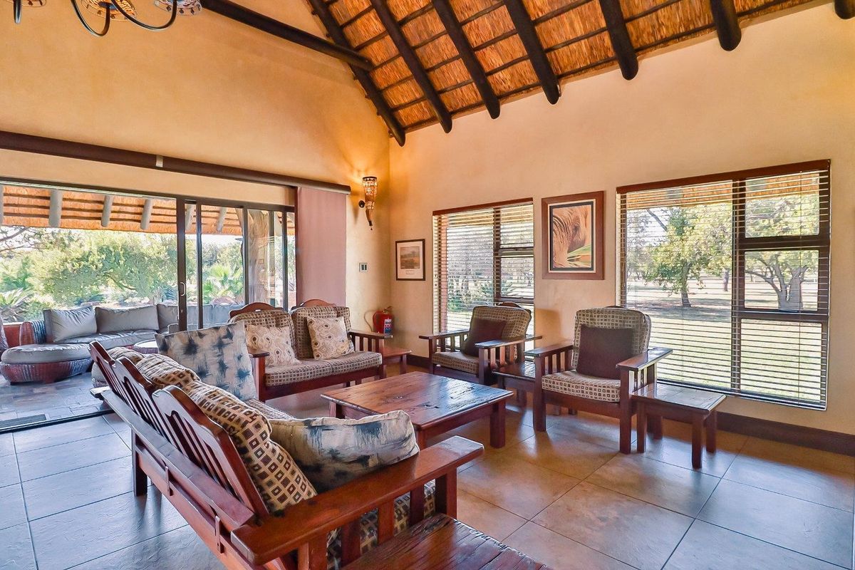 Spacious living area featuring a high vaulted thatched ceiling, tiled flooring, and large sliding doors opening onto a covered patio with garden views.