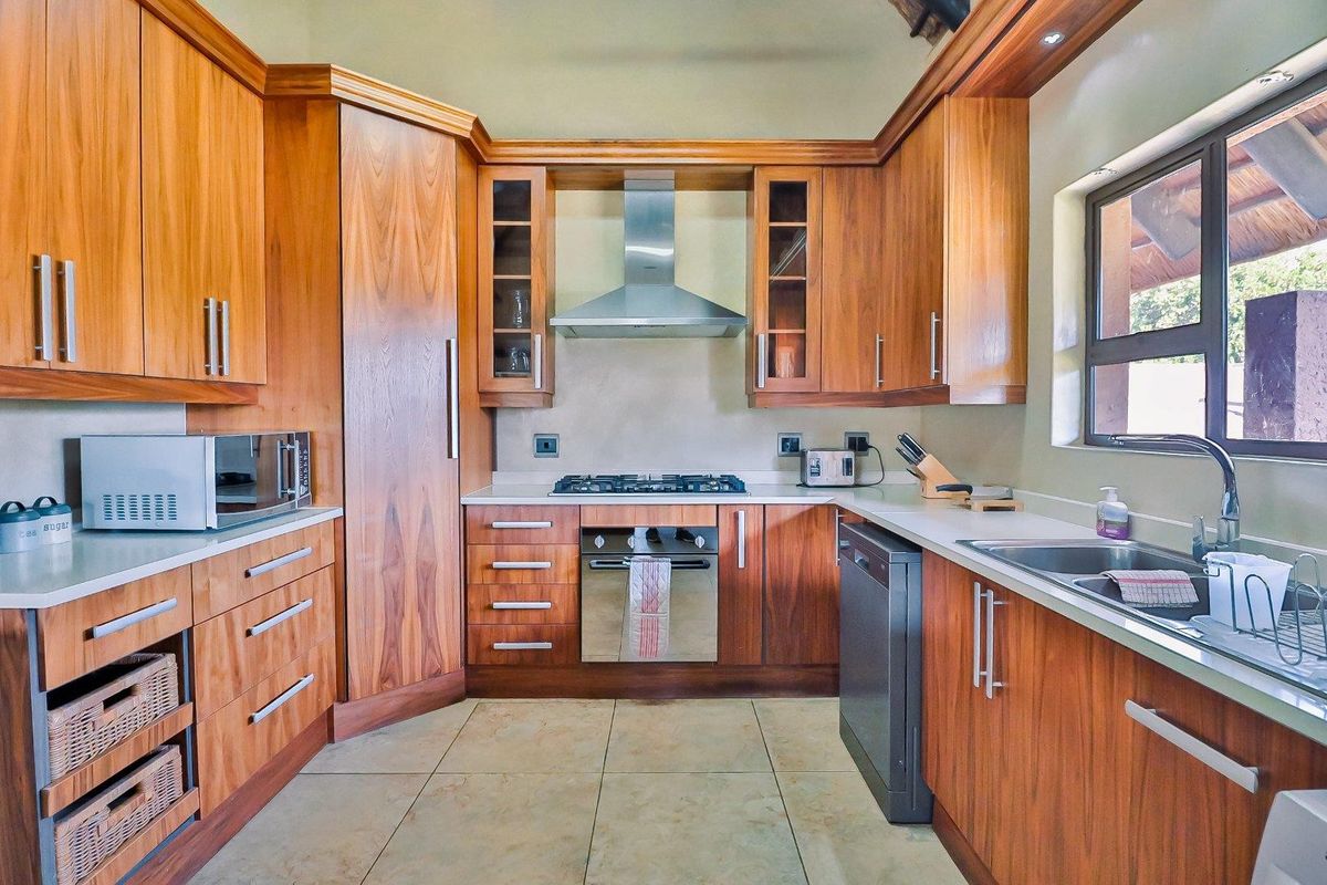A well-maintained kitchen featuring warm wood cabinetry, stone countertops, a built-in oven, gas hob, stainless steel extractor fan, and tiled flooring.