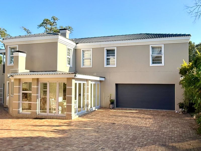 A well-maintained two-story residential property featuring a paved driveway, integrated garage, and a sunroom with large glass panel doors.