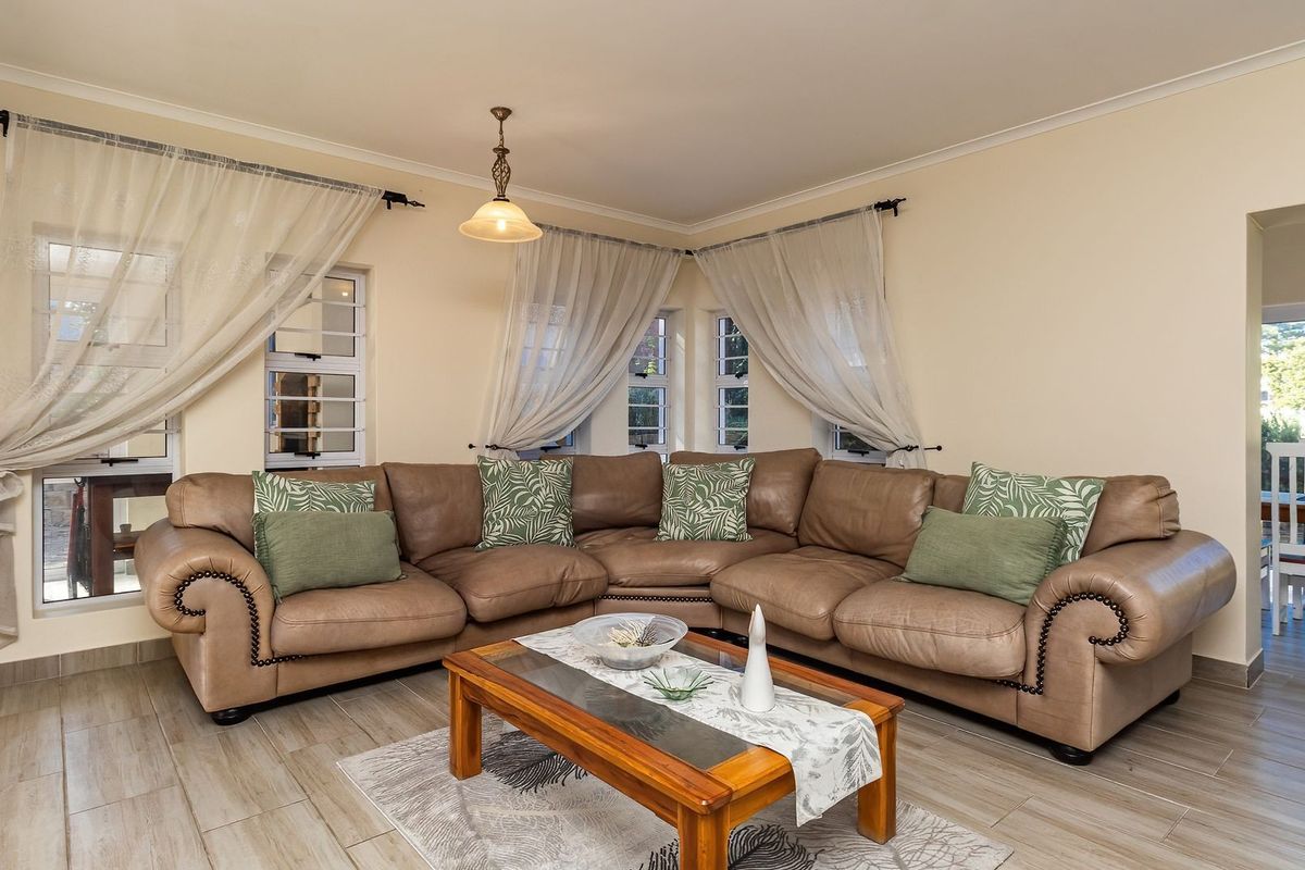 A comfortable living room featuring tiled flooring, corner windows, and a central pendant light fixture, providing a bright and inviting space.