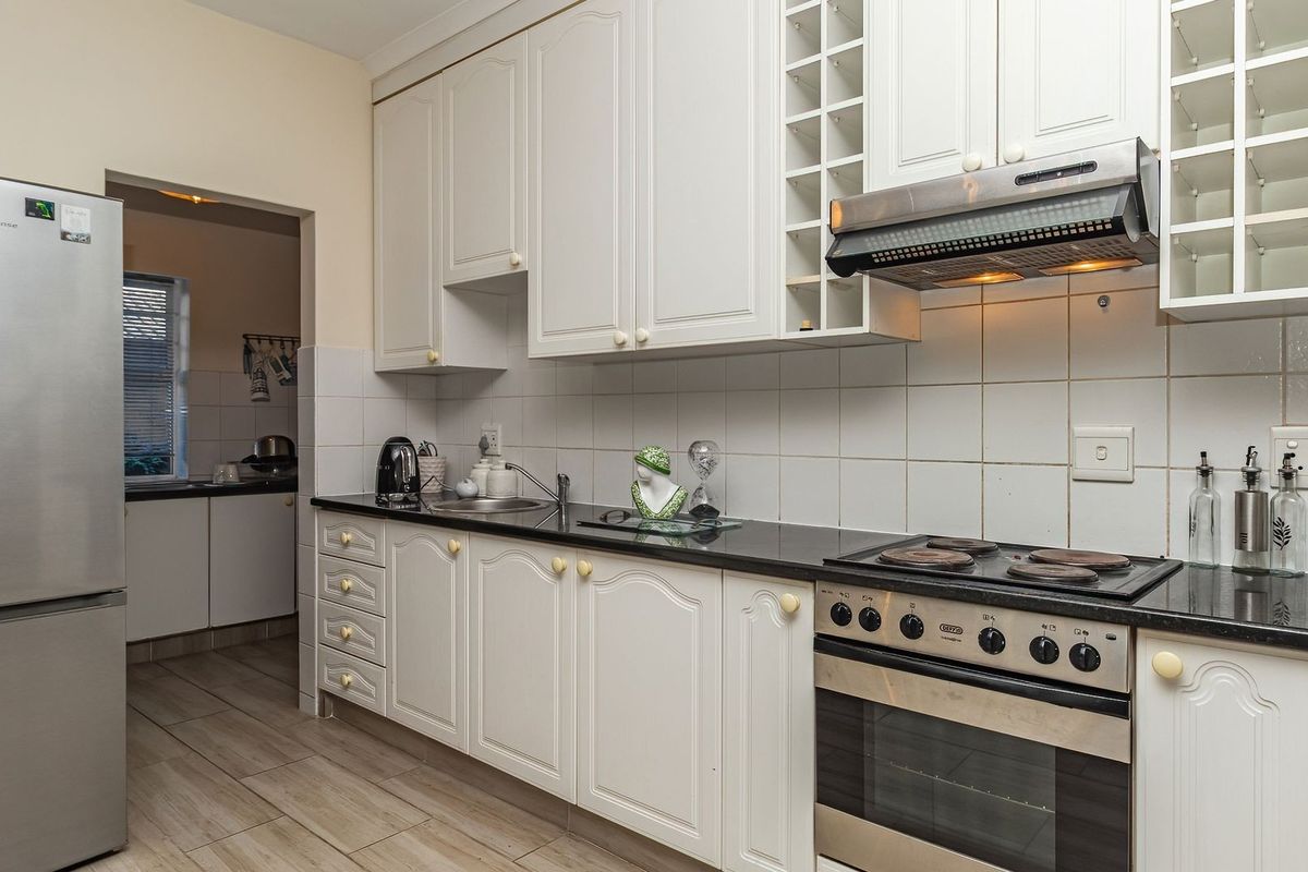 A functional kitchen featuring white cabinetry, black countertops, a built-in oven with hob, extractor fan, and tiled splashbacks, with an adjacent scullery area.