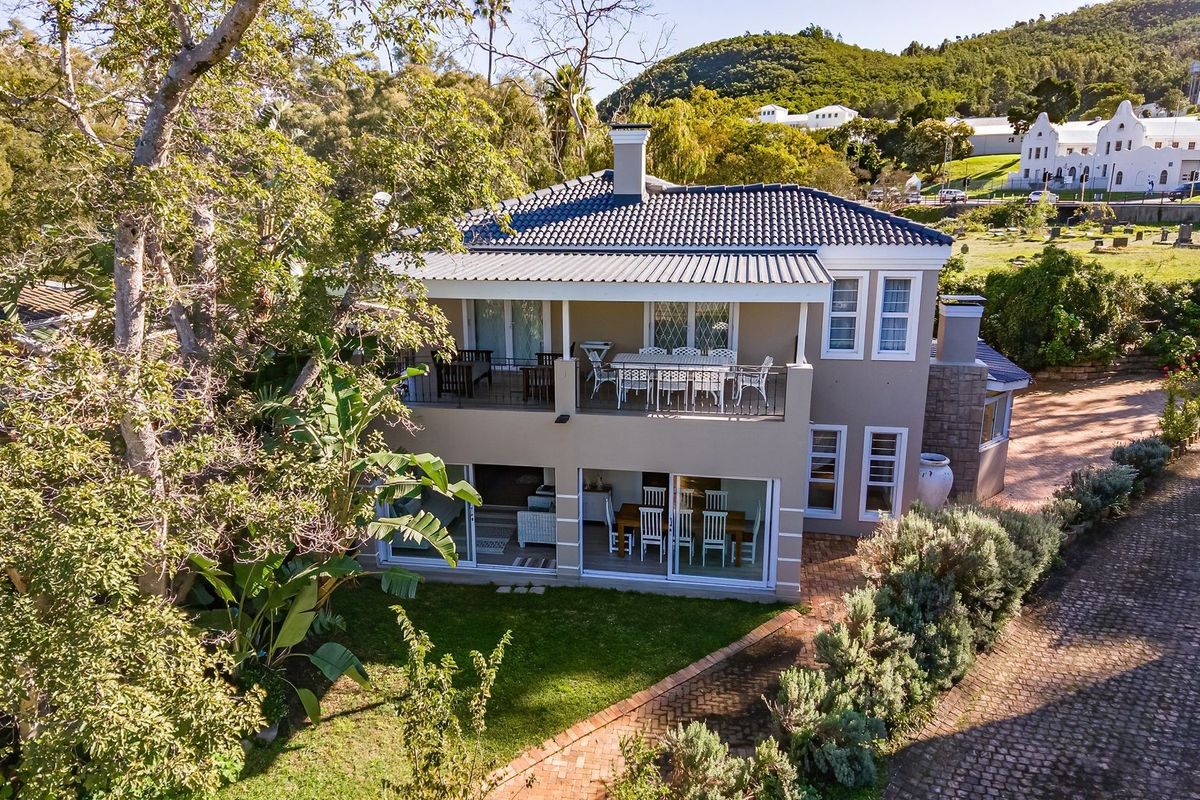 Aerial view of the rear elevation featuring a covered balcony, ground floor patio with sliding doors, and landscaped garden area.