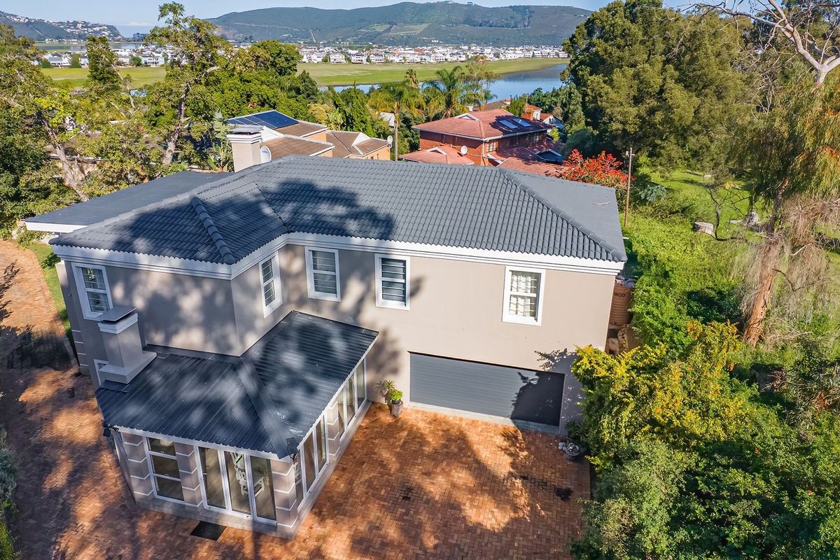 Aerial view of a two-story residential property featuring a tiled roof, brick-paved driveway, integrated garage, and a sunroom extension, set within a landscaped garden.