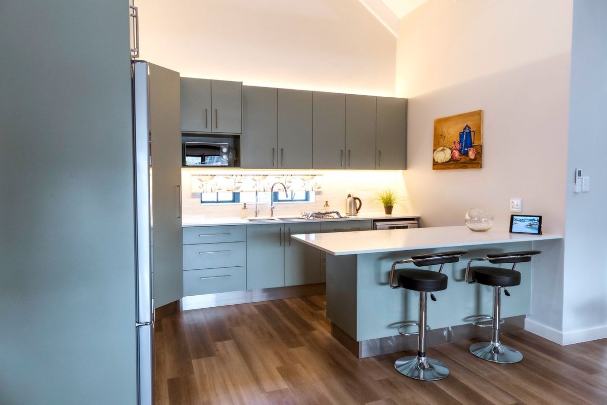 Modern kitchen featuring sage green cabinetry, stone countertops, integrated appliances, and a breakfast bar with under-cabinet lighting.