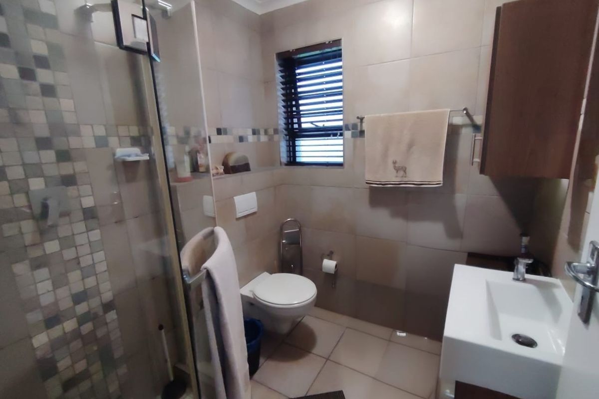 A compact bathroom featuring a glass-enclosed shower, wall-mounted toilet, and a modern vanity unit with tiled walls and flooring.
