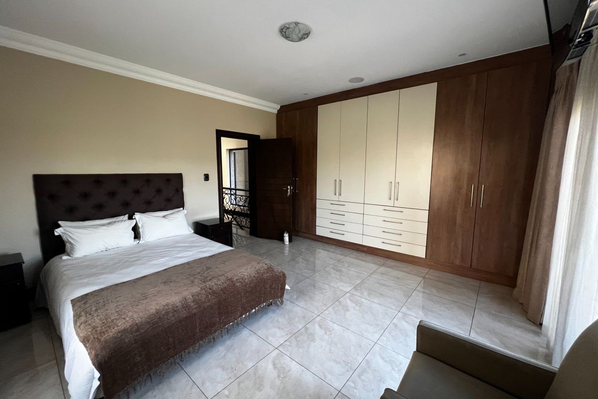 Spacious bedroom featuring large built-in wooden wardrobes with integrated drawers, tiled flooring, and recessed ceiling lighting.