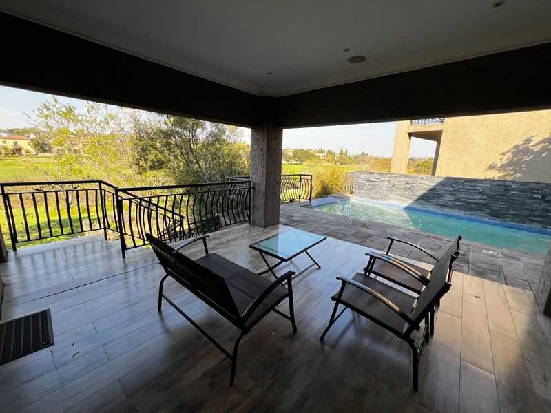 Covered patio area featuring wood-look tiled flooring, wrought iron railings, and direct access to a private swimming pool with a stone feature wall.