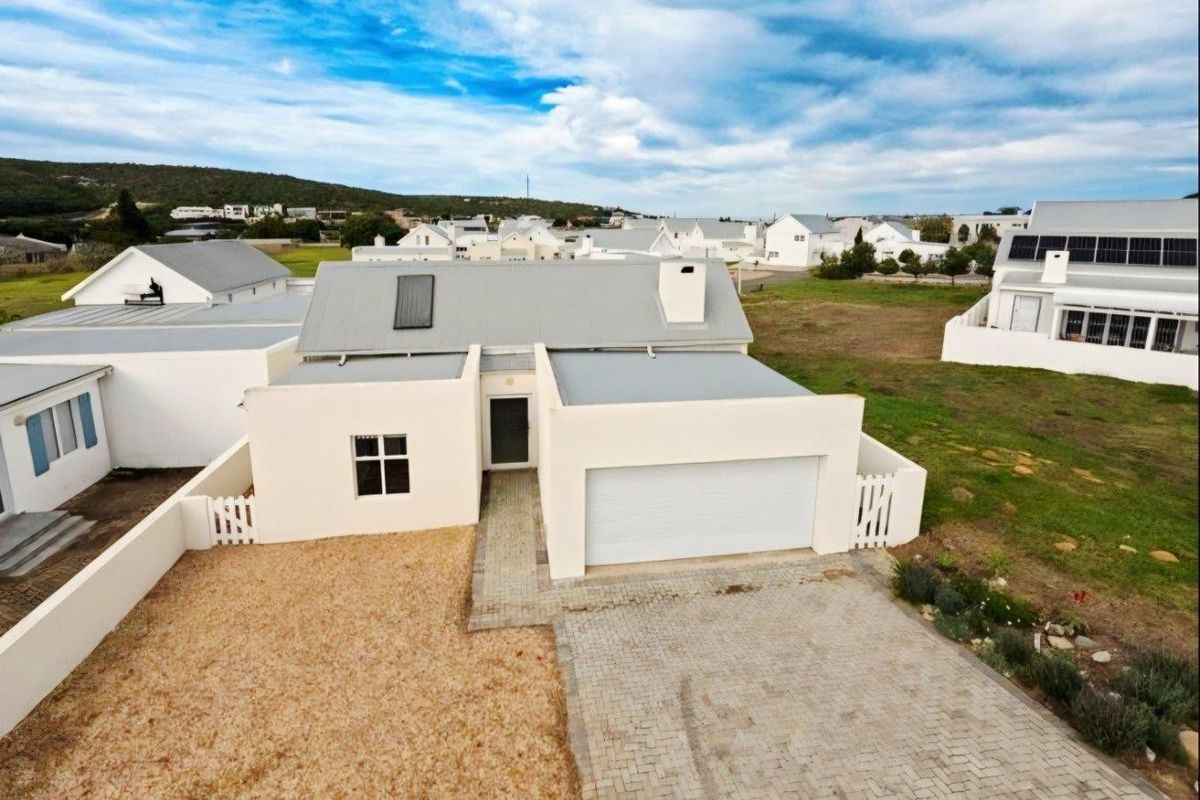 Aerial view of a modern single-story house featuring a paved driveway, attached garage, and a clean, minimalist exterior facade in a residential estate.