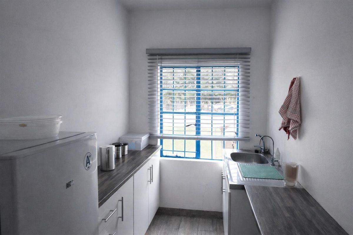 Compact kitchen area featuring built-in cabinetry, laminate countertops, a stainless steel sink, and a window with security bars.