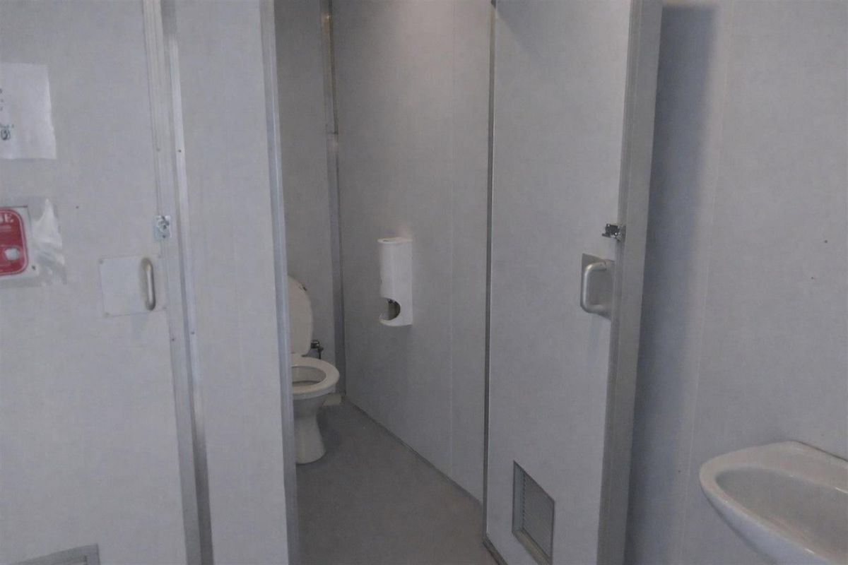 A functional industrial-style restroom facility featuring a toilet, wall-mounted paper dispenser, and a small hand basin.