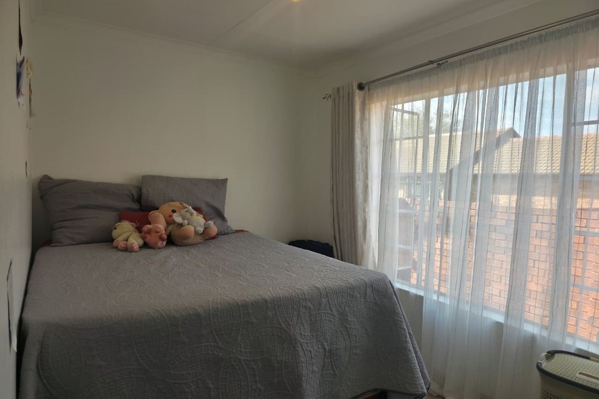A standard bedroom featuring tiled flooring, neutral walls, and large windows with curtain rails, providing natural light.