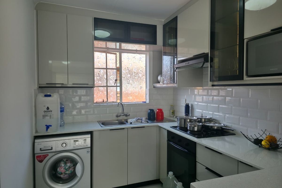 A modern, compact kitchen featuring sleek cabinetry, subway tile backsplash, integrated appliances, and a dedicated laundry space with plumbing connections.