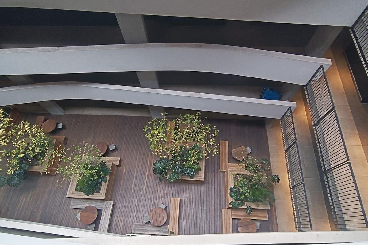 An elevated view of a modern apartment complex courtyard featuring timber decking, built-in planter boxes, and architectural concrete ramps.