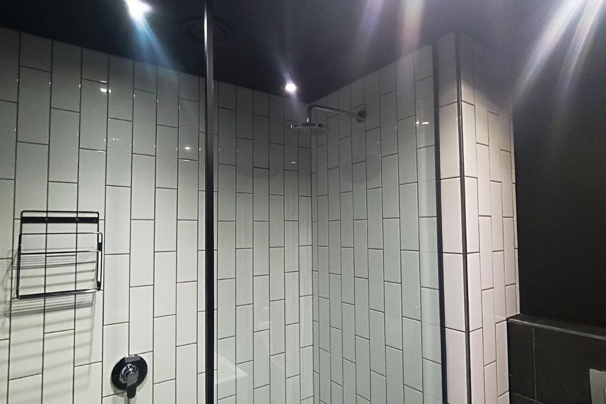 Modern walk-in shower featuring white subway wall tiles, a black ceiling, and a contemporary rainfall showerhead with a glass partition.