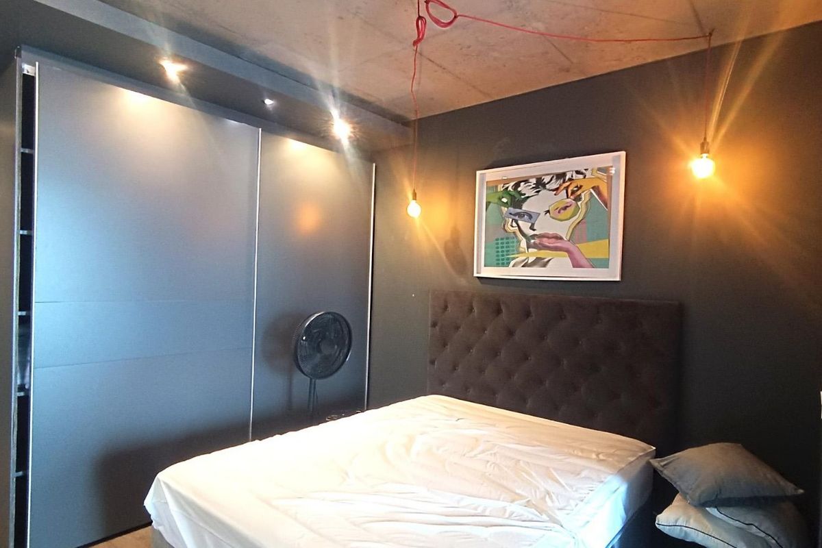 Modern bedroom featuring a raw concrete ceiling, dark accent walls, and large built-in sliding door wardrobes with integrated downlighting.